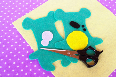 自制毛毡绿色动物套件，波尔卡圆点紫罗兰色背景上的剪刀。儿童的缝纫项目。从毛毡剪泰迪熊图案。如何使一个软的玩具在家里。一步一步