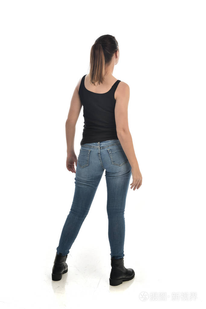 穿黑色单和牛仔裤的黑发女孩的全长肖像.站姿, 回到相机.