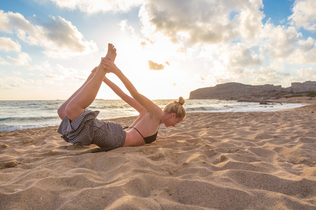 女人上练瑜伽的海滩在日落时分