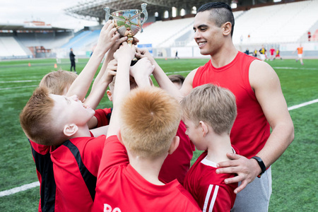 少年足球队的肖像在户外体育场赢得比赛后一起捧奖杯, 欢呼喝彩