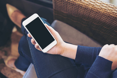 一个女人的手拿着白色的手机, 在大腿上坐在沙发上的黑色屏幕的样机