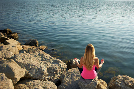在黎明时分, 在海边的大石头上瑜珈。长着金色长发的女孩, 身材苗条。放松和冥想的水。迎接新的一天