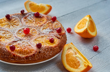 自制的橙色馅饼, 装饰着新鲜的红莓和橙色切片的灰色背景。柑橘派。侧面视图