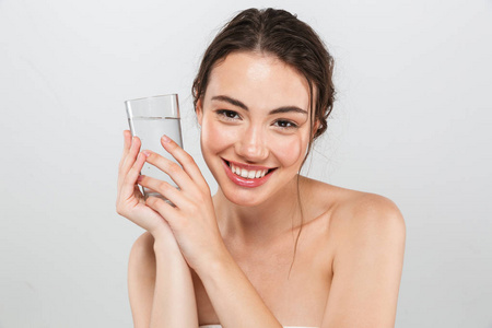 美丽的肖像, 一个快乐的年轻裸上身的女人与化妆持有玻璃水隔离在灰色背景下