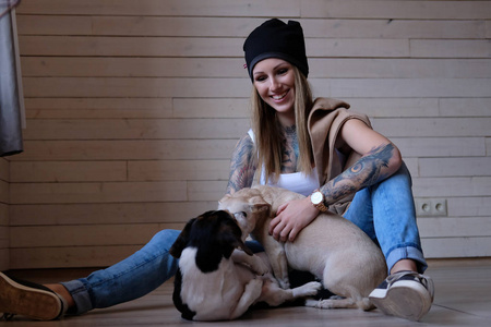 快乐的 tattoed 金发女人玩她的小狗, 而坐在木地板上