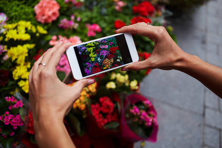 紧紧抓住手持手机的女性手在屏幕上的照片摄像头模式。女孩在户外站着, 用手机拍摄春天花朵的照片。选择性聚焦