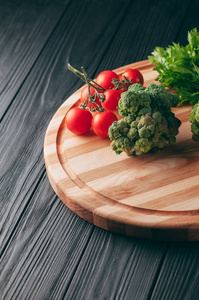 在一个黑暗的木桌上, 在一个圆木板新鲜的绿色花椰菜, 欧芹, 莳萝和樱桃西红柿为您的健康。食谱。成分。膳食食品。放置在文本之下。