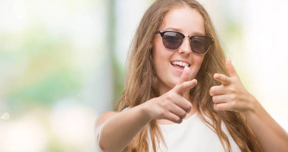 年轻的金发女郎戴着太阳镜, 手指上带着快乐和滑稽的面孔拍照。良好的能量和共鸣