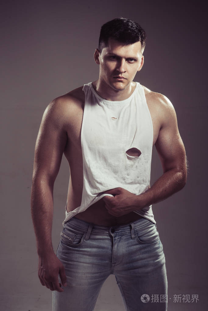 男子在性感的坦克顶部和牛仔裤的灰色背景.肌肉发达的男性和二头肌