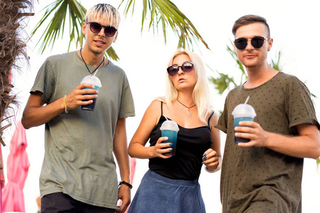 三朋友愉快的公司休息在热带海滩和喝鸡尾酒很杂志概念