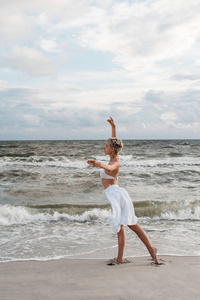 美丽的年轻金发女郎在沙滩上跳舞白色礼服