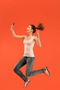 蓝色背景下的年轻女子图像在跳跃时使用笔记本电脑或 tablet 小工具