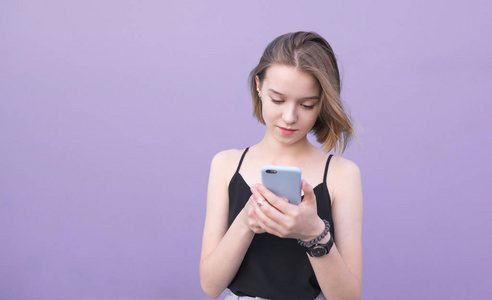 迷人的女孩使用智能手机在柔和的紫色背景。一位专注于智能手机的漂亮女孩的肖像