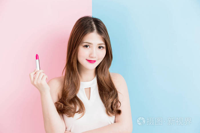 一个美丽的女孩拿着红色的口红孤立在粉红色和蓝色的背景