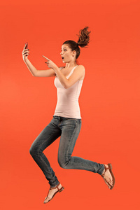 蓝色背景下的年轻女子图像在跳跃时使用笔记本电脑或 tablet 小工具