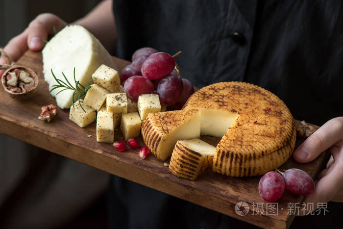 在奶酪制造商手中的质朴的美食奶酪拼盘, 关闭。各式手工制作的奶酪托盘上的手黑色背景, 复制空间
