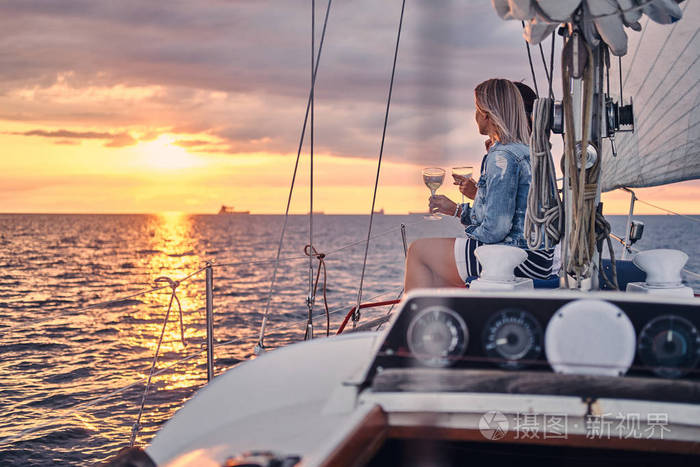 两个女朋友在游艇上放松, 手里拿着酒杯, 在公海上日落的时候