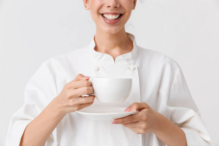 裁剪图像的一个开朗的年轻女子厨师身着制服持有杯和飞碟隔离在白色背景