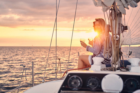 两个快乐的女性朋友在游艇上放松, 手里拿着酒杯, 在公海上日落的时候