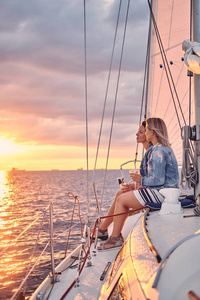 两个女朋友在游艇上放松, 手里拿着酒杯, 在公海上日落的时候