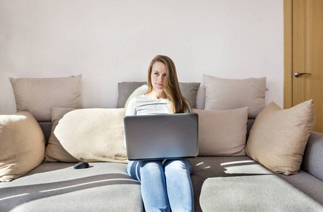穿着牛仔裤的白人妇女坐在沙发上用笔记本电脑, 年轻女子与小工具