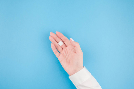 妇女手拿着白色药丸在柔和的蓝色纸背景与拷贝空间以极小的样式, 模板为文本。医疗药学医疗保健理念
