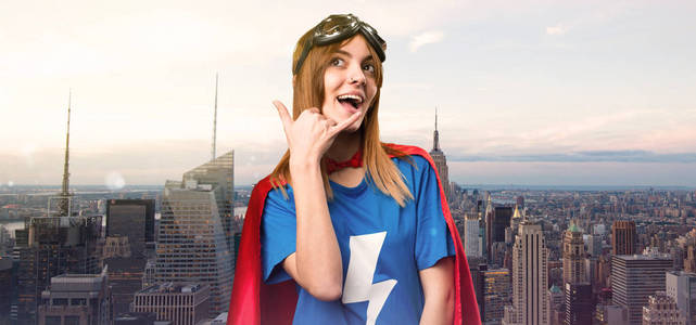 在摩天大楼城市做电话手势的漂亮超级英雄女孩