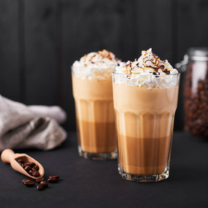 冰拿铁咖啡在一个高的玻璃与焦糖和巧克力糖浆和奶油。深色木质背景