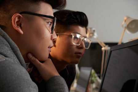 两名亚洲学生在眼镜工作在计算机显示器