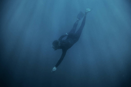 运动的青年男子 freediver 穿着潜水衣和鳍潜水水下在蓝色的深海