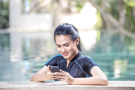 年轻的亚洲妇女使用她的智能手机在池畔