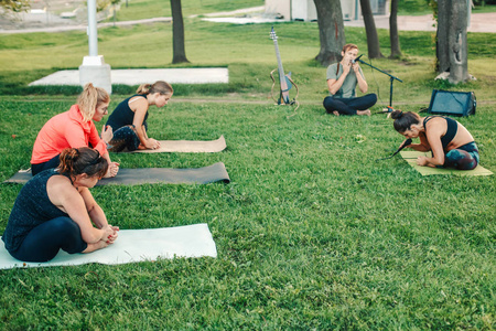 一群白种人在公园外面做瑜伽在日落。女性伸展运动, 户外锻炼。健康生活方式的现代活动。体育教学训练课