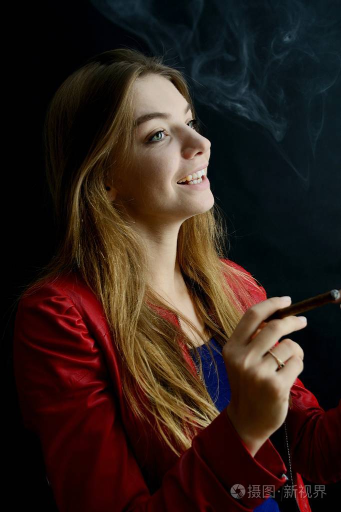 年轻女性吸烟 cigarillo.黑色背景红色夹克的妇女
