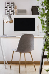 灰色椅子在书桌与台式计算机和灯在现代白色工作空间内部。真实照片