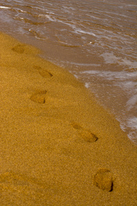 沙子上的一串光秃秃的脚印。海浪在海边, 沙滩上。海水中的泡沫。夏季时间