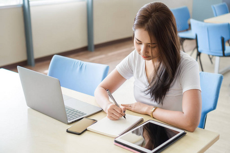在笔记本电脑和平板电脑在图书馆,教育和研究概念桌边坐着写字照片