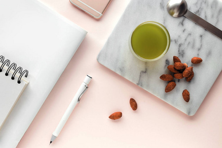 创意平坦的工作空间, 风格最小。现代办公桌与健康小吃杏仁和一杯绿茶在柔和的粉红色背景, 顶部视图