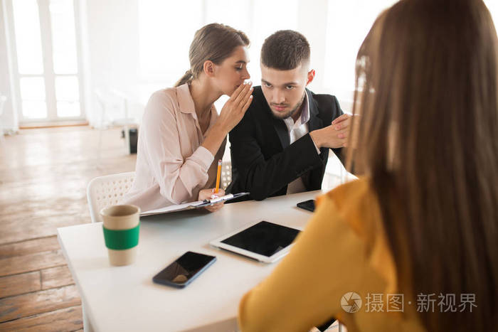 年轻的企业妇女与文件夹在手耳语对商人附近花费工作面试在现代办公室