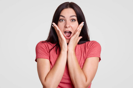 情绪化的黑发年轻女性保持手上的脸颊, 张开嘴, 表达 surprisement