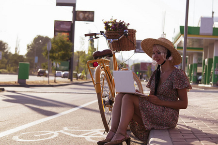 可爱的女孩在帽子看起来笔记本电脑在一个城市的街道和自行车