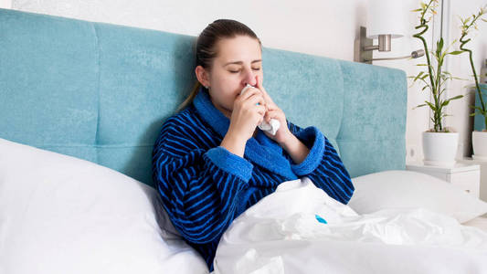生病的年轻妇女的肖像躺在床上使用鼻腔喷雾