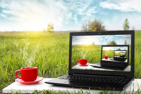 笔记本电脑和杯热咖啡上背景风景如画的大自然,室外办公室照片
