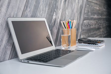 侧视图的笔记本电脑上创意设计师桌面与水玻璃，计算机鼠标 计算器和文具项木制板背景。小样