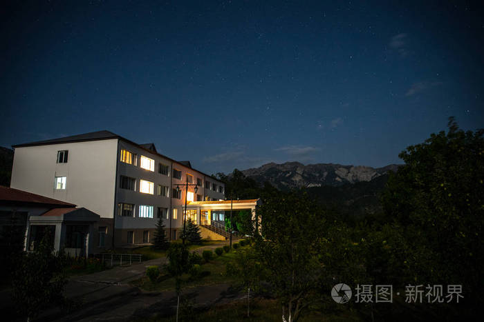 晚上在森林里建筑的山夜风景与月亮或老式乡下房子在晚上与云彩和星.
