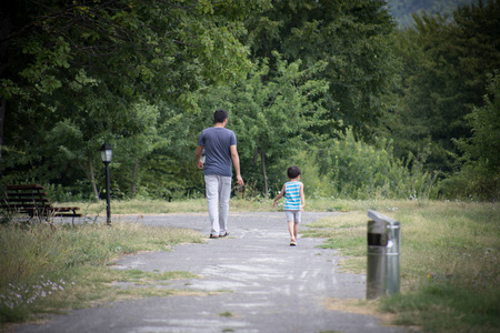 小男孩和他的父亲享受温暖的夏日。年轻的父亲和他的小儿子走在公园的道路上