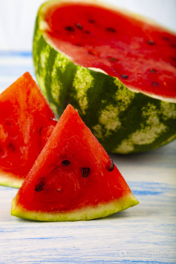 一块西瓜放在一张蓝色的木桌上.美味的甜点在木碗里