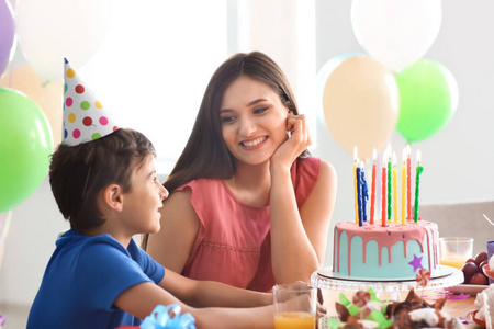 可爱的小男孩和他的母亲在桌与生日蛋糕