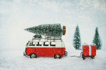 复古圣诞明信片背景小型古董车在屋顶上运载圣诞树和礼物 礼品盒 在雪冬林