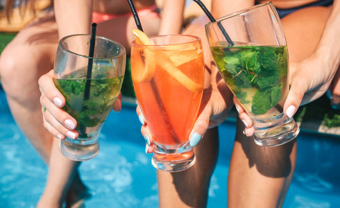 三张五颜六色的鸡尾酒的图片妇女掌握在手里。他们坐在游泳池边, 把腿放在水里。
