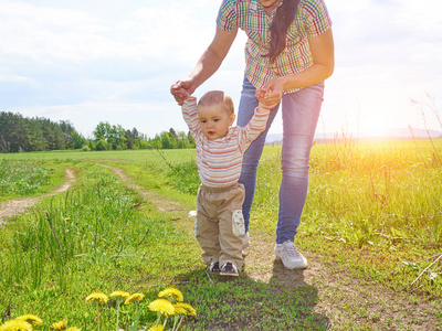 妈妈教走年轻的儿子可爱的女孩跳跃牵手与父母走在阳光明媚的公园, 全